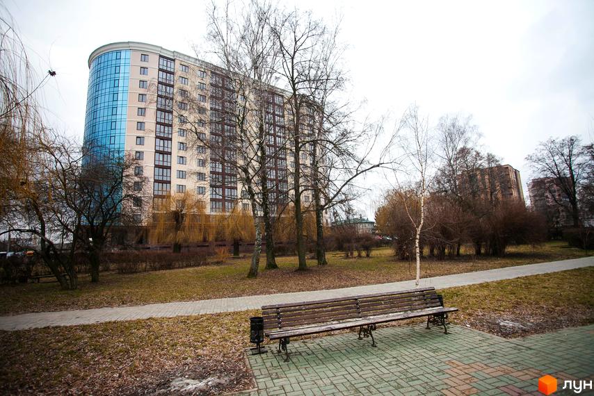 Зображення багатоповерхового будинку в ЖК Paradise. На передньому плані лавка та тротуарна плитка.