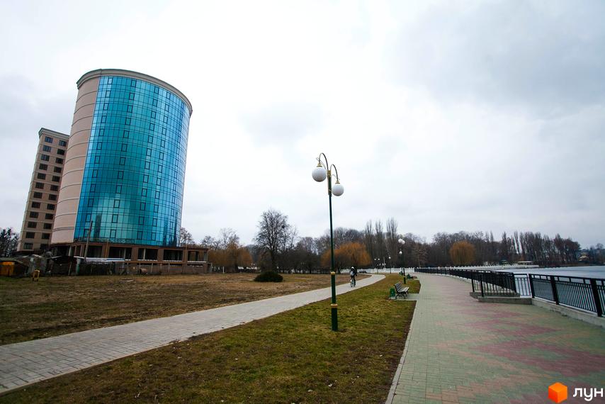 Зображення фасаду та прибудинкової території Житлового комплексу Paradise. Висотна будівля з великими вікнами, поруч пішохідна алея та дерева.