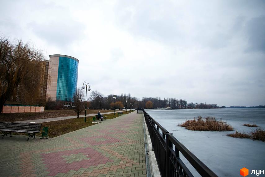 Зображення Житлового комплексу Paradise. Вид на будівлю з блакитними вікнами та набережну з замерзлим озером.