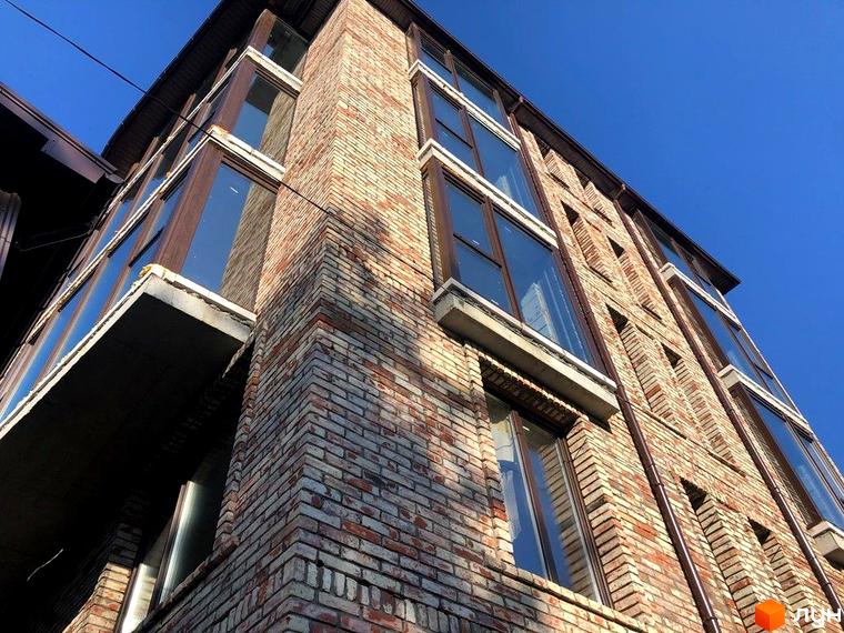 Зображення цегляного фасаду Клубного будинку „Чернишевського 20“ з великими вікнами на тлі блакитного неба.