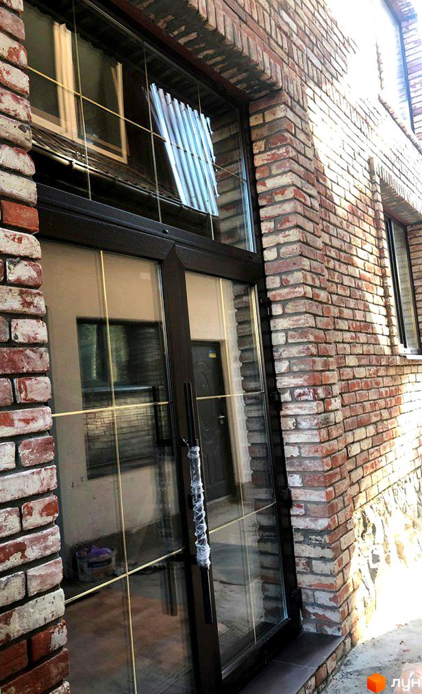 Фасад Клубного будинку Чернишевського 20 з червоної цегли, великими вікнами та скляними дверима. Видно бруківку біля входу.