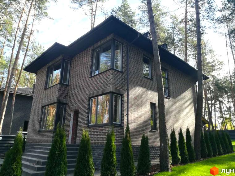 Котеджне містечко КМ Realist: двоповерховий будинок з цегляним фасадом та великими вікнами, оточений зеленими насадженнями та деревами.