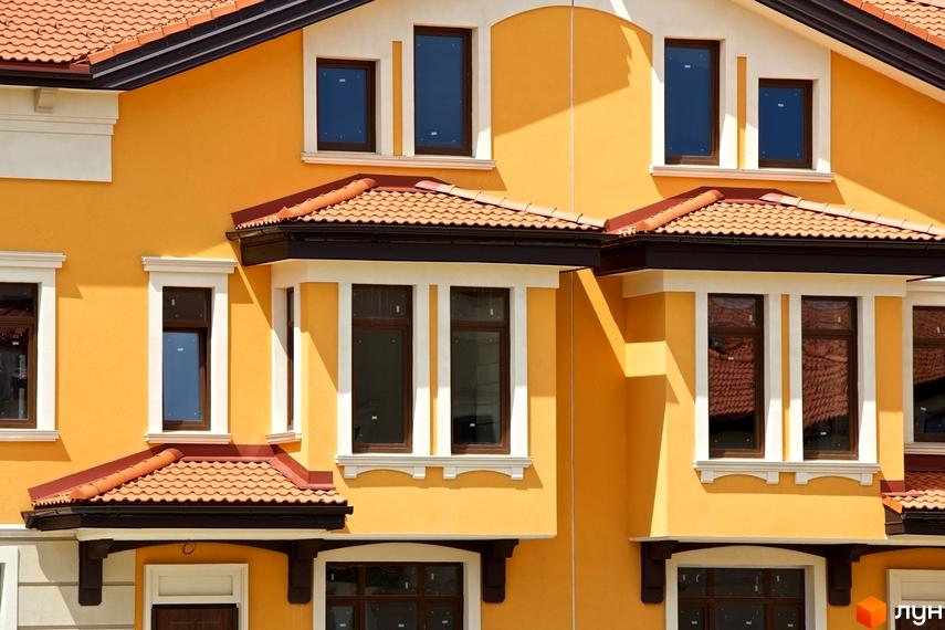 Фасад будинку житлового комплексу КМ Італійський квартал. Будинок має жовтий колір стін, червоний черепичний дах та коричневі вікна. Білі декоративні елементи підкреслюють архітектуру будівлі.