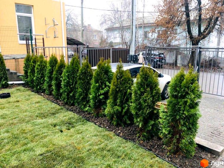 Зовнішній вигляд клубних будинків „На Генерала Пушкіна“ з зеленими насадженнями вздовж огорожі. На задньому плані видно припарковані автомобілі.