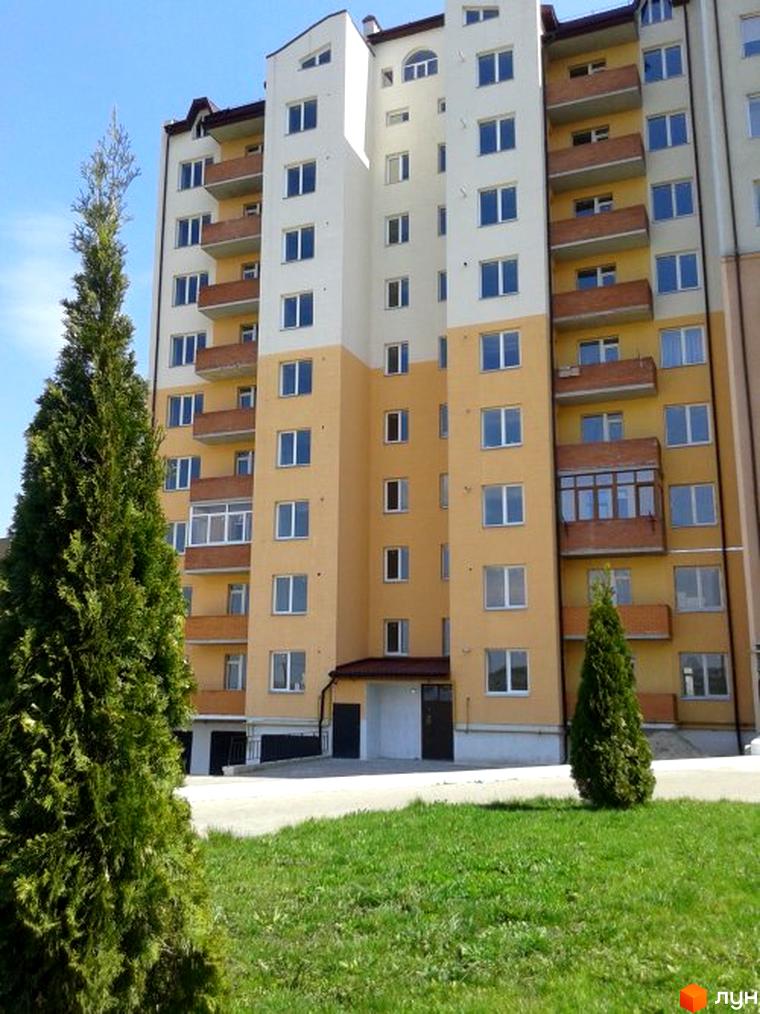 Зовнішній вигляд новобудови на вул. Коновальця, 4а, 4б. Будинок має жовто-білий фасад з балконами та вікнами. Поруч зелена галявина та дерева.