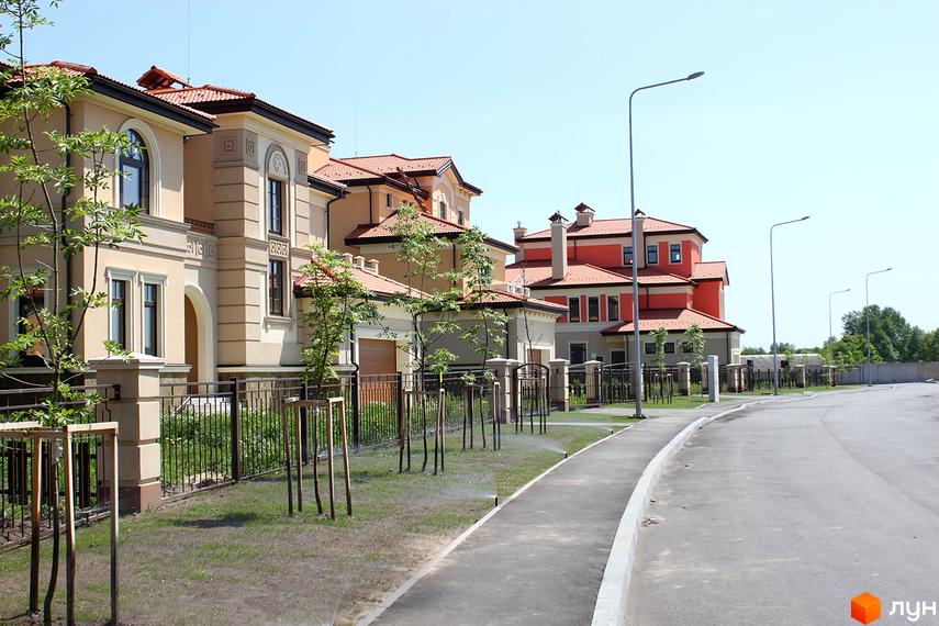 Котеджне містечко Італійський квартал: фасади будинків у світлих тонах з червоними черепичними дахами. Доглянута прибудинкова територія з доріжками та молодими деревами.