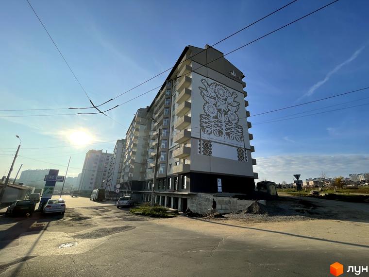 Багатоповерховий житловий будинок на вул. Горбачевського з великим декоративним розписом на фасаді. Навколо будинку дорога та ділянка з будівельними матеріалами.