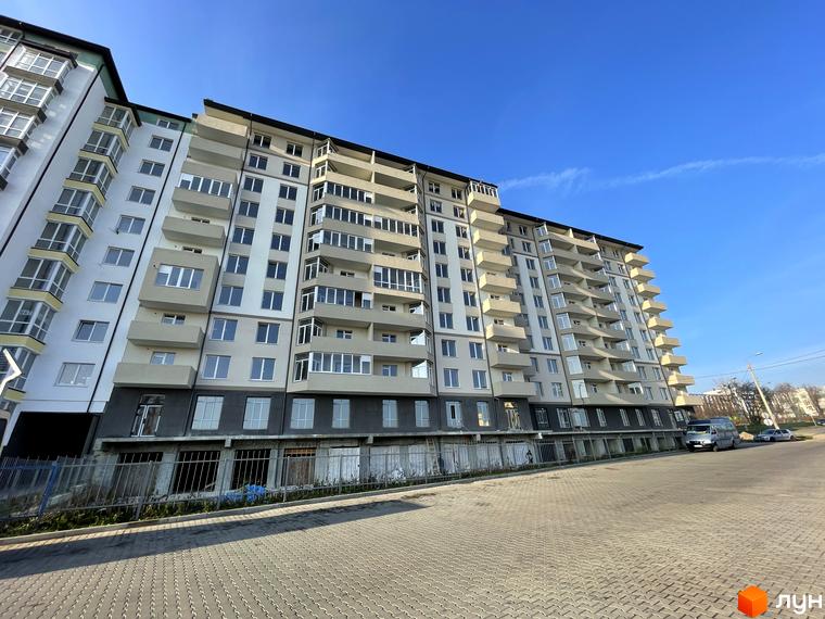 Фасад багатоповерхового житлового комплексу на вул. Горбачевського зі світлими стінами та балконами. Перед будинком бруківка.