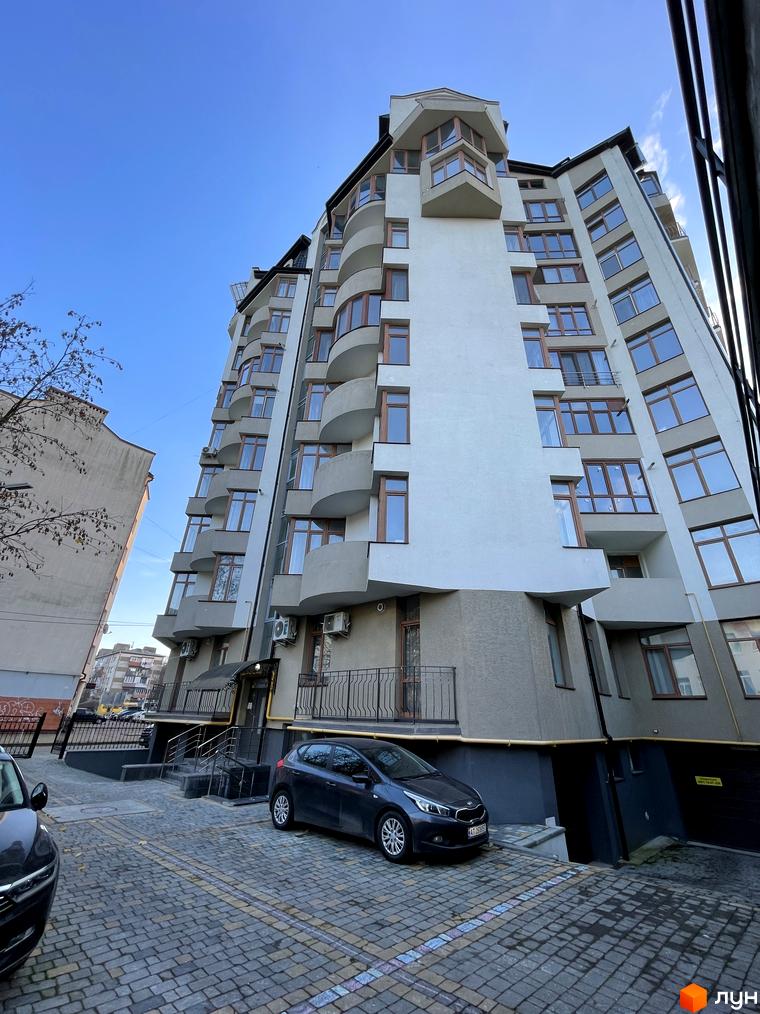Фото фасаду багатоповерхового будинку за адресою вул. Короля Данила, 20. На передньому плані припаркований автомобіль та тротуарна плитка.