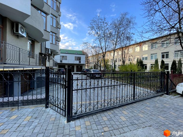 Вигляд фасаду будинку на вулиці Короля Данила, 20. На передньому плані кована огорожа та вимощена бруківкою прибудинкова територія.