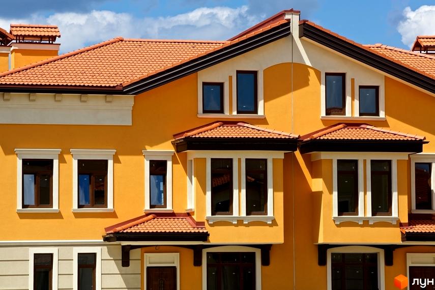 Зовнішній вигляд фасаду будинку житлового комплексу КМ Італійський квартал з помаранчевим дахом та жовтими стінами. На фасаді багато вікон з коричневими рамами.