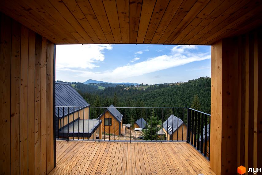 Вигляд з тераси Котеджного містечка SKOGUR на дерев'яні котеджі з темними дахами та зелені пагорби вдалині.