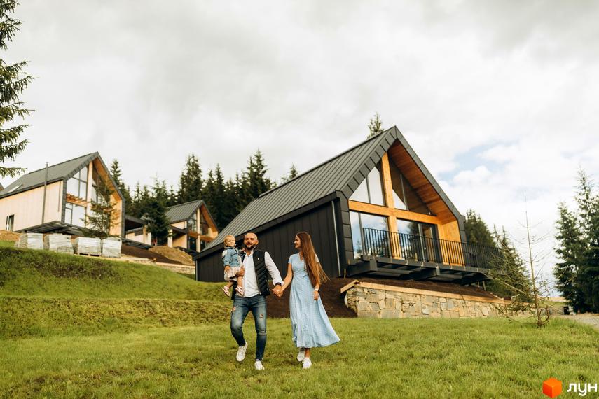 Сім'я гуляє біля котеджів у Містечку котеджів SKOGUR. Будинки з великими вікнами та чорним дахом на зеленій галявині.