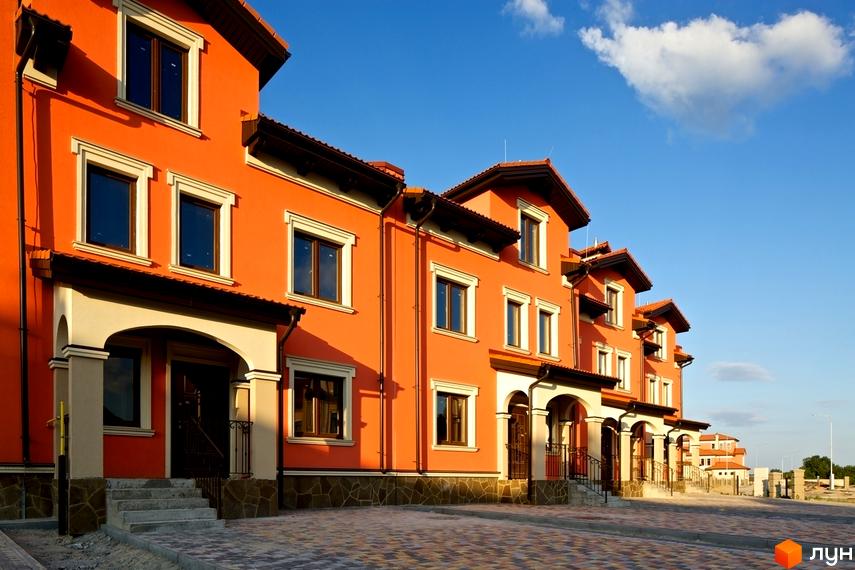 Котеджне містечко КМ Італійський квартал. Оранжеві фасади будинків з коричневими дахами та білими віконними рамами. Перед будинками вимощена бруківкою прибудинкова територія.
