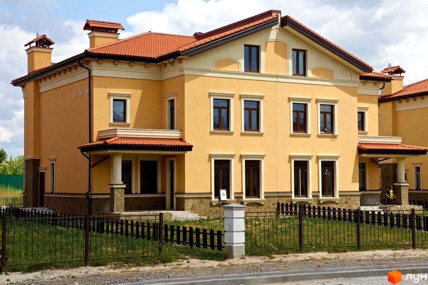 Котеджне містечко КМ Італійський квартал. Фасад будинку в жовтих тонах з червоною черепичною кришею. Огороджена територія з зеленою травою та парканом.