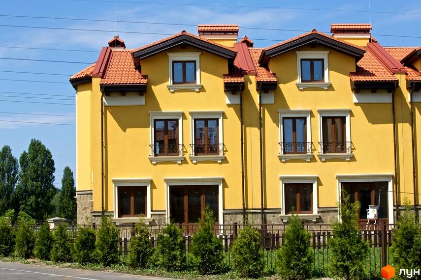 Котеджне містечко Італійський квартал: фасади яскраво-жовтих будинків з червоними черепичними дахами та зеленими туями перед парканом.