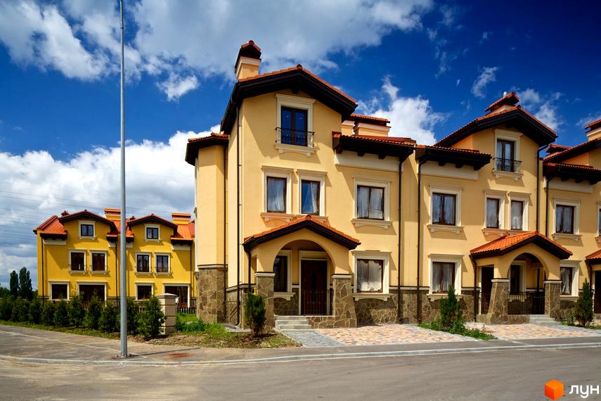 Котеджне містечко КМ Італійський квартал: жовті двоповерхові будинки з червоними дахами та кам'яним оздобленням цоколя. Прибудинкова територія з доглянутими зеленими насадженнями та бруківкою.