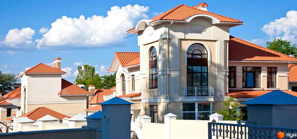 Зображення житлового будинку в Котеджному містечку Oasis з червоним дахом та світлими стінами. На передньому плані видно огорожу та стовпчики.