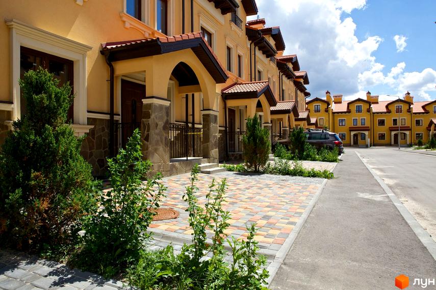 Котеджне містечко КМ Італійський квартал. Фасади будинків виконані в жовтому кольорі з червоною черепицею та кам'яним оздобленням. Прибудинкова територія вимощена плиткою та озеленена.