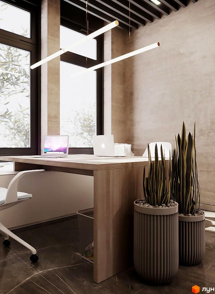 Інтер'єр офісу з робочим столом, двома ноутбуками та рослинами у горщиках. Освітлення забезпечують підвісні світильники.