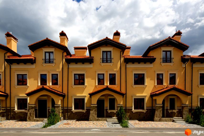 Котеджне містечко КМ Італійський квартал. Фасади жовтих будинків з червоними дахами. Прибудинкова територія з бруківкою та зеленими насадженнями.