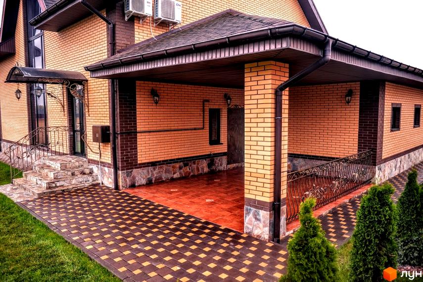 Вигляд фасаду будинку в Котеджному містечку Розкішне з цегляною кладкою та облаштованою прибудинковою територією з тротуарною плиткою.