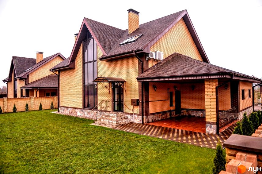 Зображення будинку з жовтої цегли з коричневим дахом у Котеджному містечку Розкішне. Навколо будинку зелений газон.