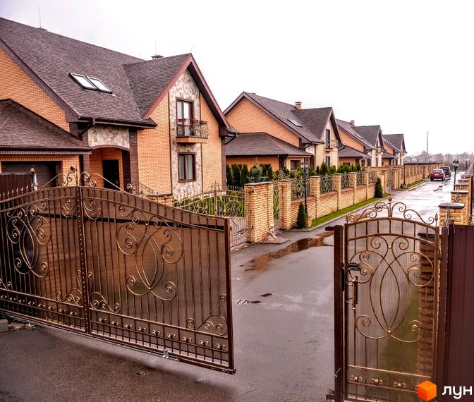 Вигляд Котеджного містечка Розкішне з вулиці. Цегляні будинки з коричневими дахами та металевими воротами.