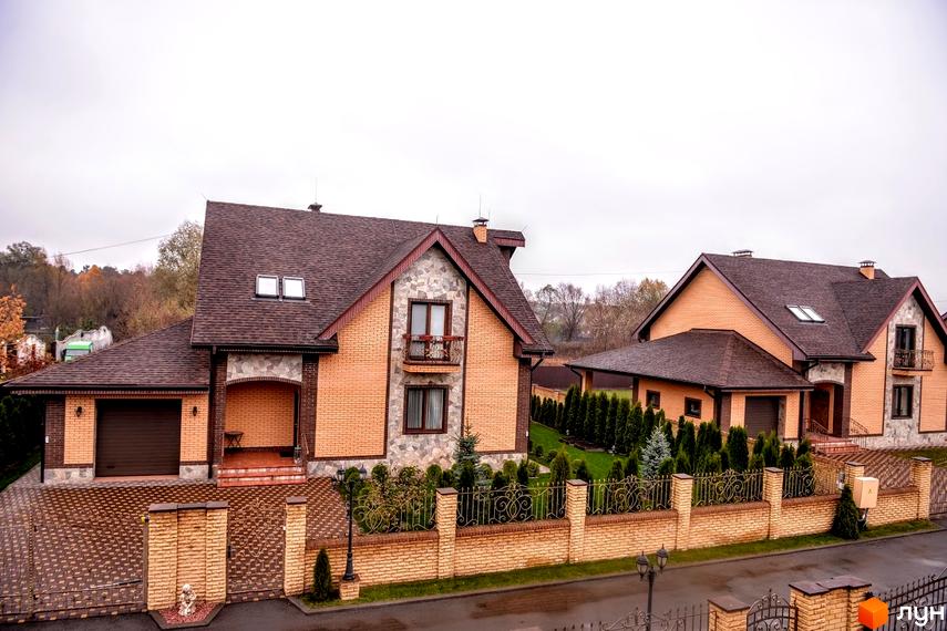 Вигляд Котеджного містечка Розкішне з двоповерховими будинками з цегли та коричневими дахами. Навколо будинків зелені насадження та огорожа.