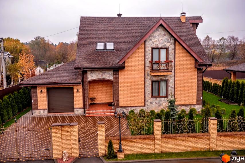 Вигляд котеджу в Котеджному містечку Розкішне з коричневим дахом та цегляними стінами. Навколо будинку зелені насадження та доглянутий газон.