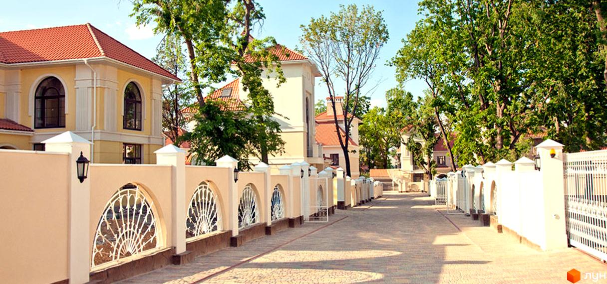 Зображення фасаду будинку в котеджному містечку Oasis. На території видно декоративну огорожу з кованими елементами та бруківку.
