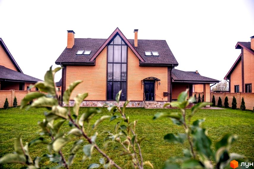 Зображення будинку в Котеджному містечку Розкішне з червоної цегли з великим вікном та зеленим газоном перед ним.