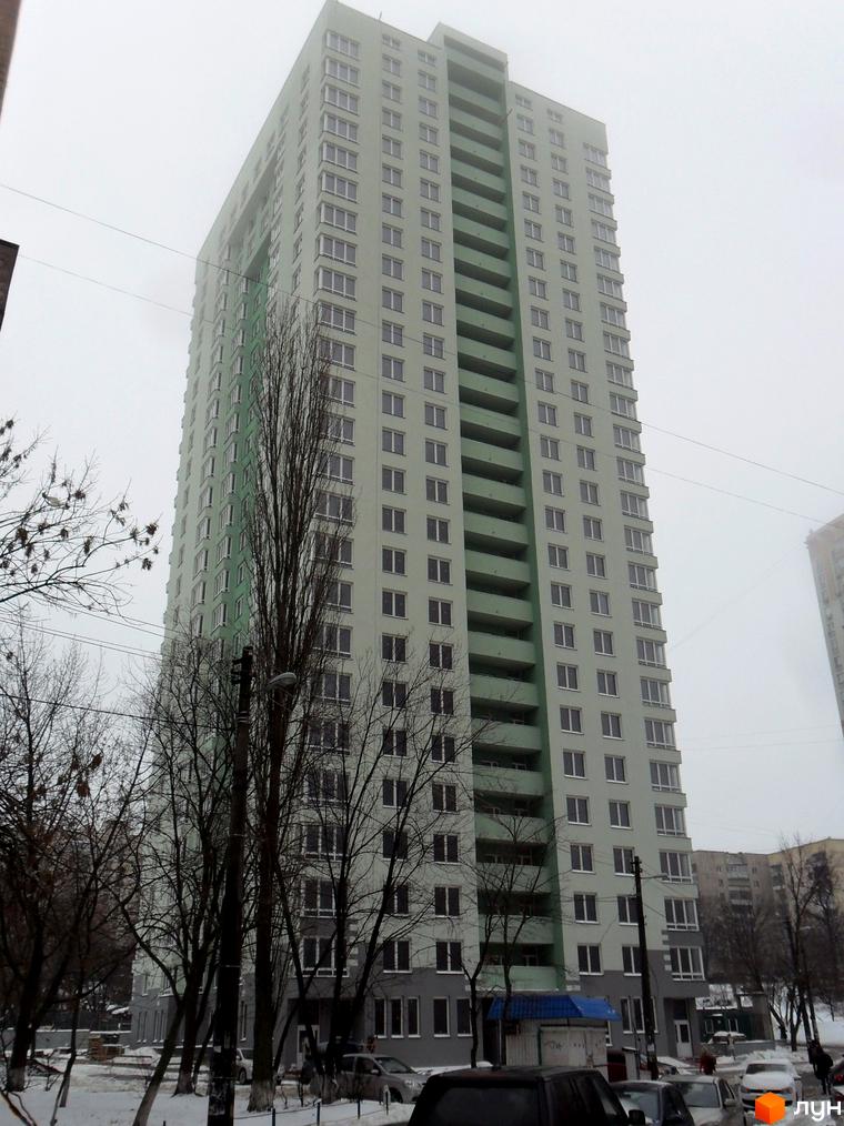 Високий житловий комплекс на вул. Феодосійська, 2 (є, ж, з, і), світло-зеленого кольору з темними балконами. Прибудинкова територія засніжена, видно дерева та авто.