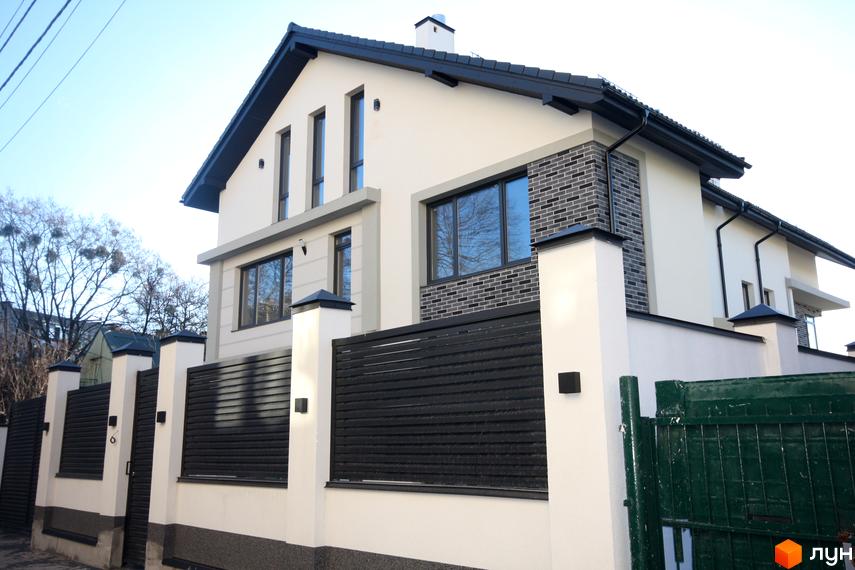 Фасад будинку Дуплекс „Чорна Перлина“ з темним дахом та вікнами, огороджений парканом з чорними ламелями.