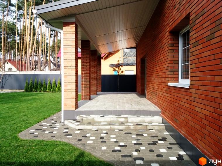 Котеджне містечко Pine Wood • mini: цегляний будинок з навісом та бруківкою на території. Зелена галявина та дерева навколо.