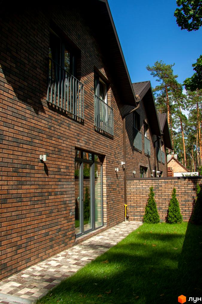 Таунхаус „На Кочубея“ з цегляним фасадом та зеленим газоном. Будівельний проєкт розташований серед соснового лісу.