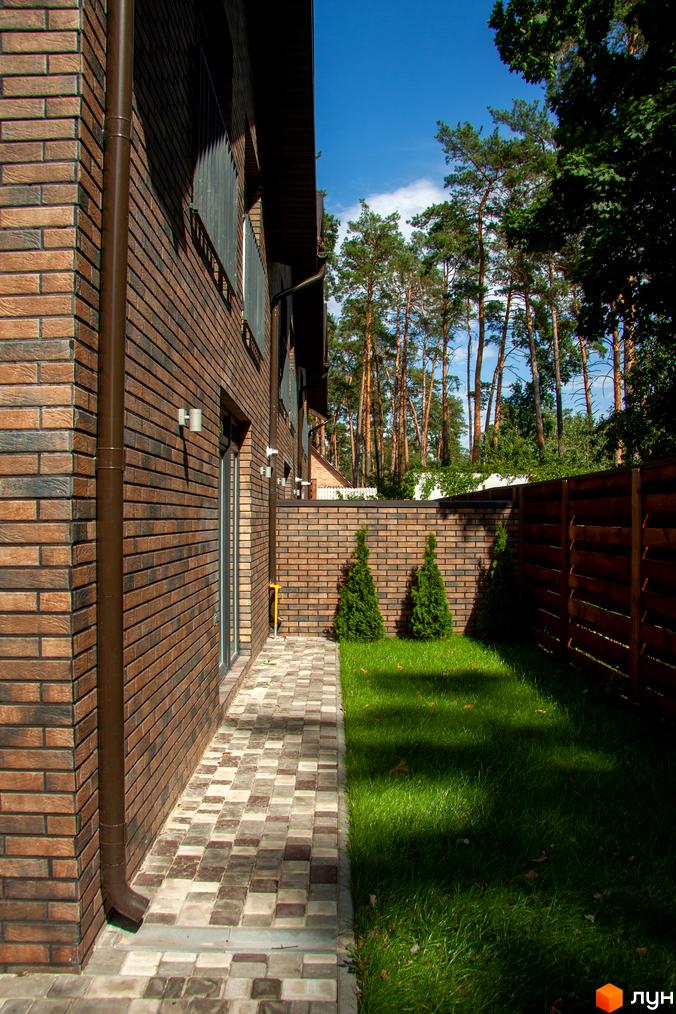 Таунхаус „На Кочубея“ з цегляним фасадом та доглянутою прибудинковою територією з газоном і бруківкою.