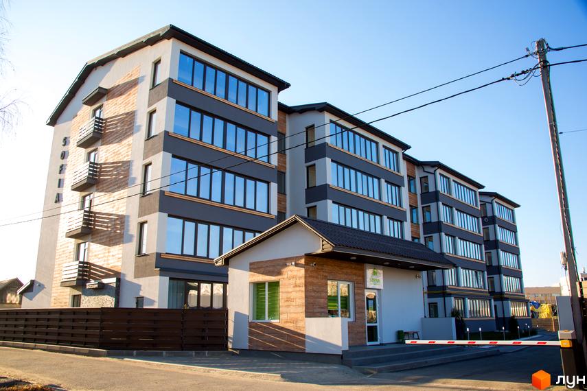 Зовнішній вигляд Житлового комплексу Софія, багатоповерховий будинок з великими вікнами та балконами. На передньому плані вхідна група.