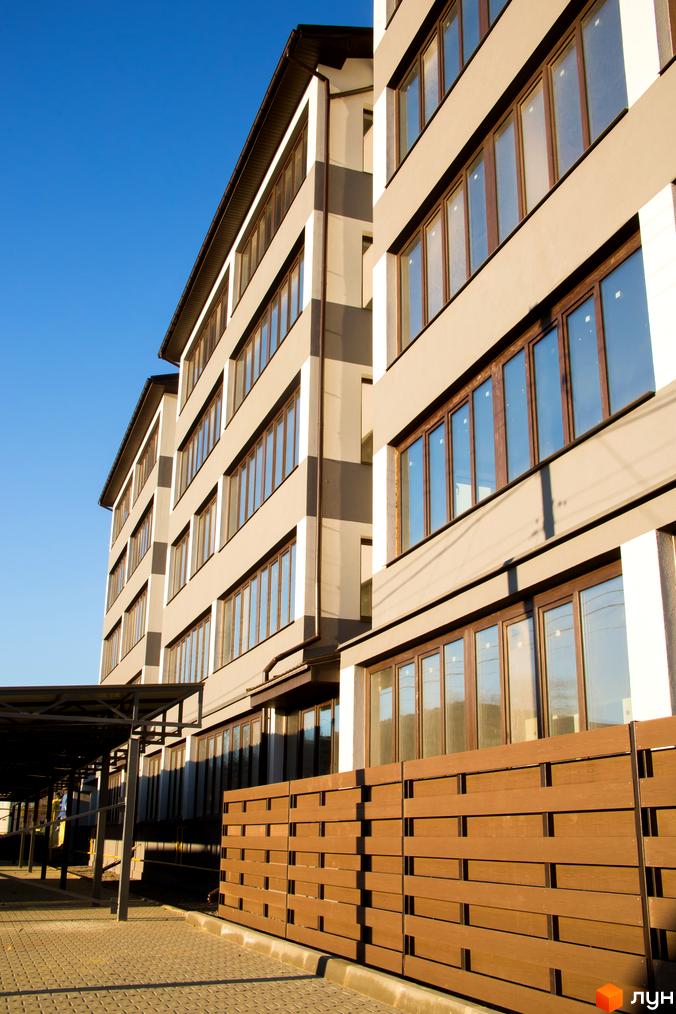 Висотна будівля ЖК Cофія з великими вікнами та коричневим парканом, сонячний день, блакитне небо. Вид на прибудинкову територію.