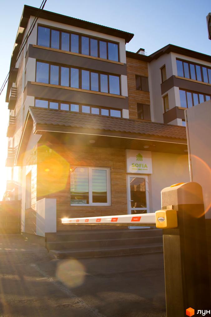 Зовнішній вигляд будівлі ЖК Софія з великими вікнами та автоматичним шлагбаумом на в'їзді. Світла будівля з темними елементами фасаду.