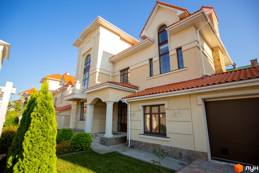 Зовнішній вигляд котеджного містечка Oasis з бежевими стінами та черепичним дахом. На прибудинковій території газон та зелені насадження.