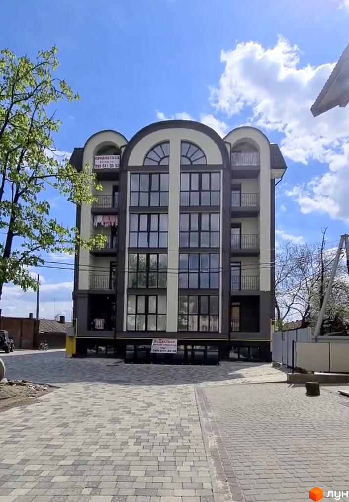 Фасад новобудови на вул. Грушевського, 35 з великими вікнами та балконами. Перед будинком вимощена бруківкою прибудинкова територія.