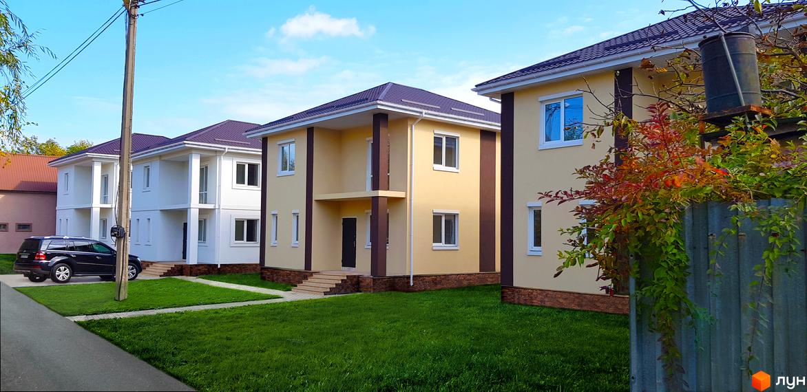 Котеджне містечко КМ Garden House: двоповерхові будинки світло-жовтого та білого кольору з коричневими колонами та дахом. Доглянута прибудинкова територія з газоном та доріжками.