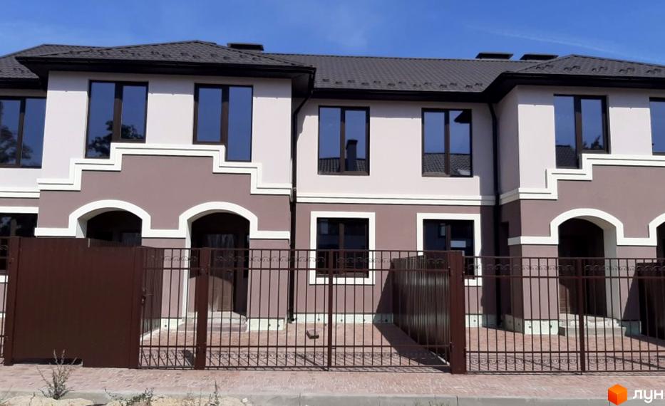 Котеджне містечко КМ Сонячний будинок: двоповерхові будинки з коричневим дахом, великими вікнами та арками, огороджені парканом. Навколо будівель - доглянута територія.