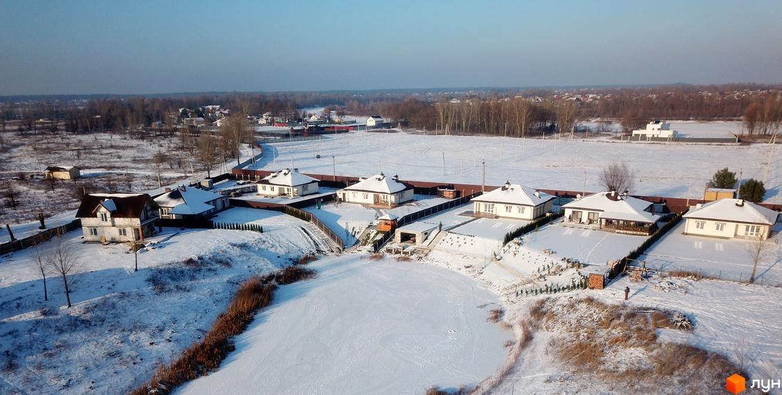 Котеджне містечко КМ Маєток взимку. Сучасні котеджі з білими стінами та темними дахами, розташовані на засніженій ділянці біля водойми.