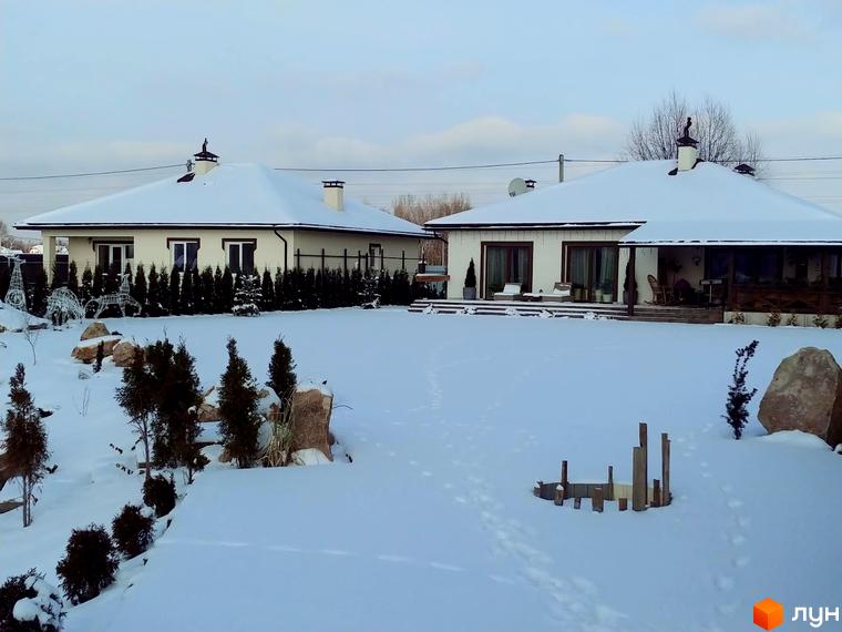 Котеджне містечко КМ Маєток. Два білих будинки під снігом з вікнами та дверима, накриті білими дахами. Навколо будівель зелені ялинки та засніжена територія.