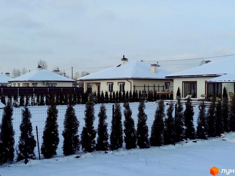 Котеджне містечко КМ Маєток. Будинки з білими стінами та темними дахами під снігом, огороджені парканом з туями. Зимовий пейзаж.