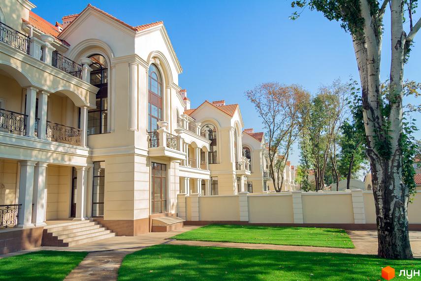 Зображення житлового комплексу Королівські сади. На фото видно будівлі з білими фасадами, червоними дахами та балконами. Поруч газон та дерева.