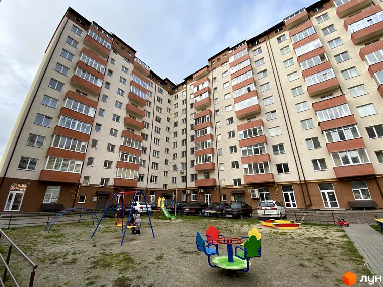 Зовнішній вигляд багатоповерхового будинку на вулиці Стуса та Миколайчука. На подвір'ї дитячий майданчик з гойдалками та каруселлю.