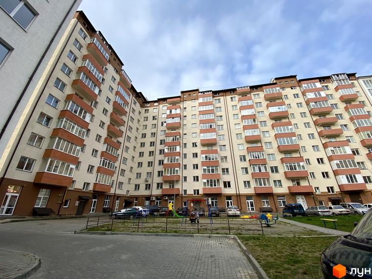 Фото фасаду житлового будинку на вул. Стуса / вул. Миколайчука. На території є дитячий майданчик, парковка та тротуарна плитка.